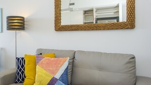 Un sofá beige con almohadones de colores y un espejo con marco de tejido en la pared.