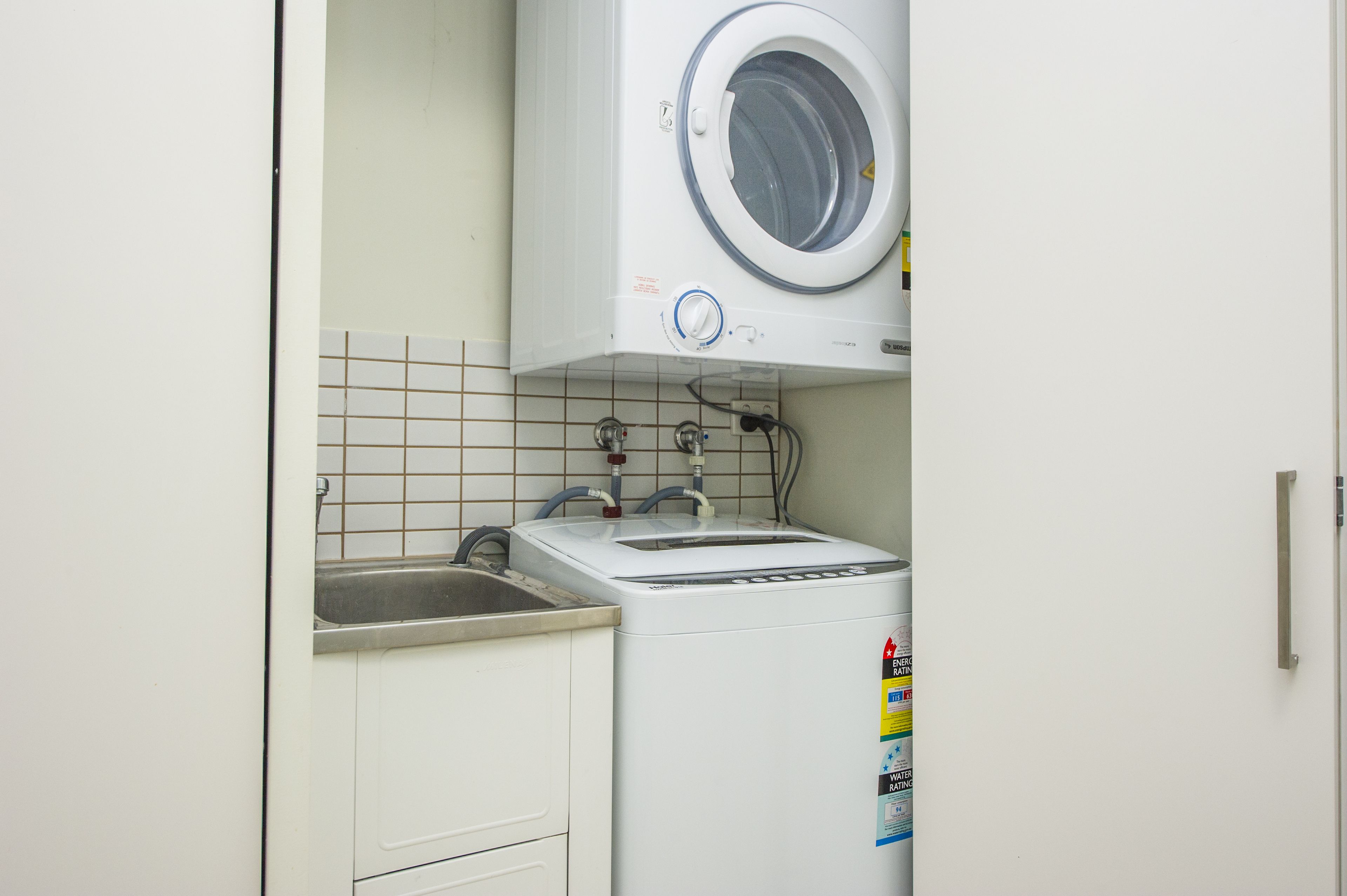 A compact laundry area with a washing machine and dryer, a sink, and tiled walls.