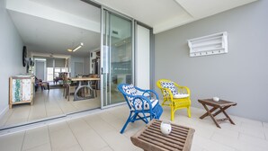 Una sala moderna con un vidrio corredero que da a una cocina, dos sillones estampados, una pequeña mesa de madera y un equipo de aire acondicionado blanco instalado en la pared.