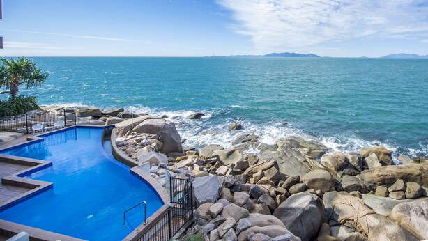 Una piscina de diseño curvo, rodeada de grandes rocas y vista al mar.