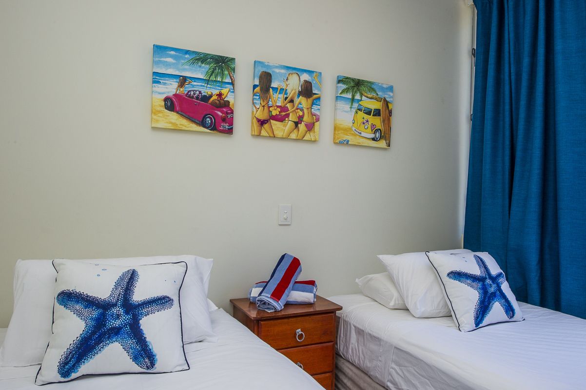 Habitació d'hotel amb dos llits, cadascun amb una almofada en forma d'estrella de mar, una tauleta de nit de fusta i tres quadres amb temàtica marina a la paret.