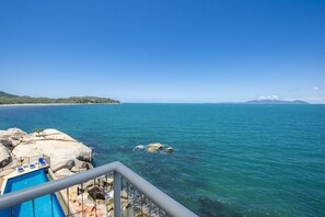 A pool area with clear blue water, a rocky shoreline, and a distant view of a beach and mountains. - 1 Bright Point Apartment 5301 (Nelly Bay)