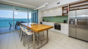 Eine moderne Küche mit einer großen Kochinsel, einem Edelstahlkühlschrank und Blick aufs Meer.