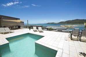 Un espace piscine aménagé sur le toit, avec des chaises longues et une vue sur la mer.