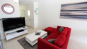 Un salon moderne avec un téléviseur à écran plat, un canapé rouge, une table basse blanche et un tableau accroché au mur.