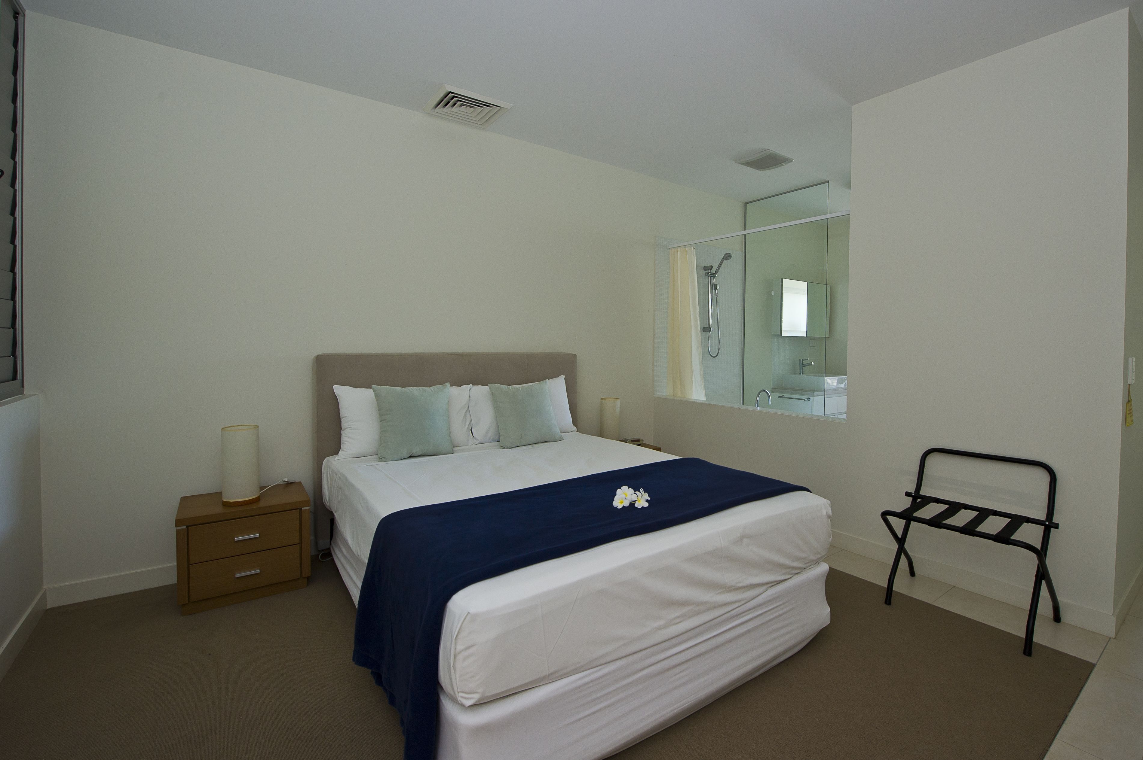 A bedroom with a bed, bedside table, nightstand, and a black metal rack.