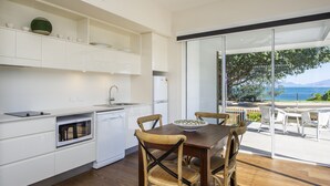 A modern kitchen with white cabinetry, a dining table with four chairs, and a view of the sea through large sliding glass doors. - Reflections Villa 1 (Picnic Bay)