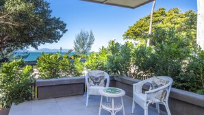 A balcony with two wicker chairs and a small table, overlooking a body of water and greenery. - Reflections Villa 1 (Picnic Bay)