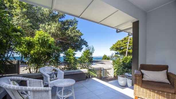 A covered patio with wicker furniture, a cushioned bench, and potted plants. - Reflections Villa 2 (Picnic Bay)
