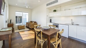 A modern kitchen with white cabinets, a dining table with four chairs, and a built-in oven. - Reflections Villa 2 (Picnic Bay)