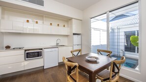A modern kitchen with white cabinetry, a built-in oven, and a dining area with a wooden table and chairs.