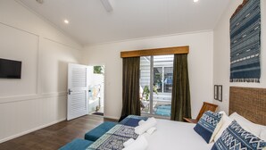 A hotel room with a large bed, two bedside tables, a TV mounted on the wall, and a sliding glass door leading to a balcony. - Reflections Villa 4 (Picnic Bay)
