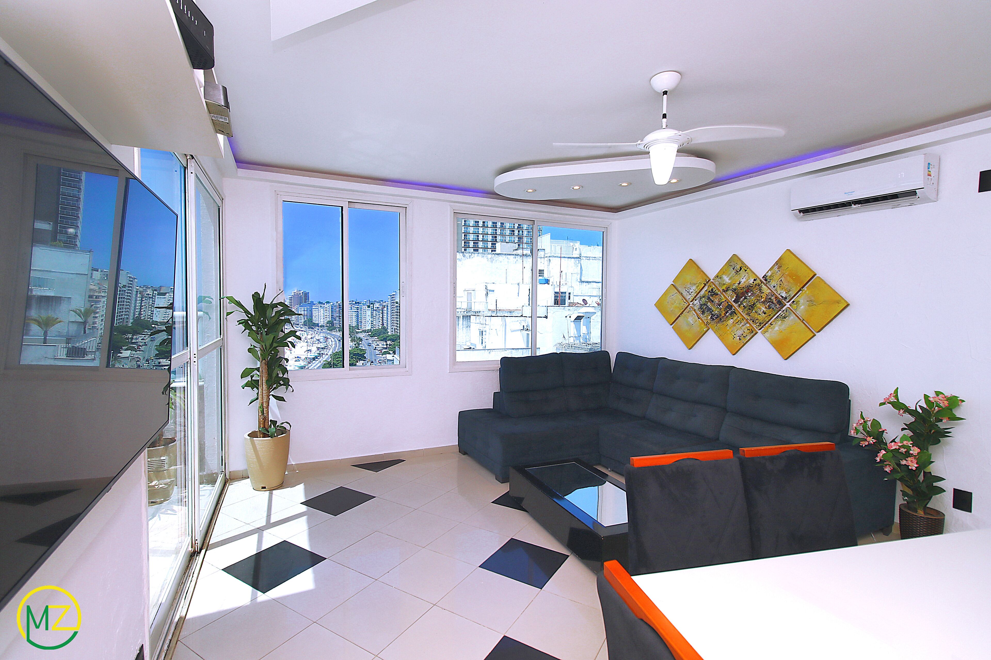 A modern living room with a sofa, a coffee table, and a view of the city through large windows.