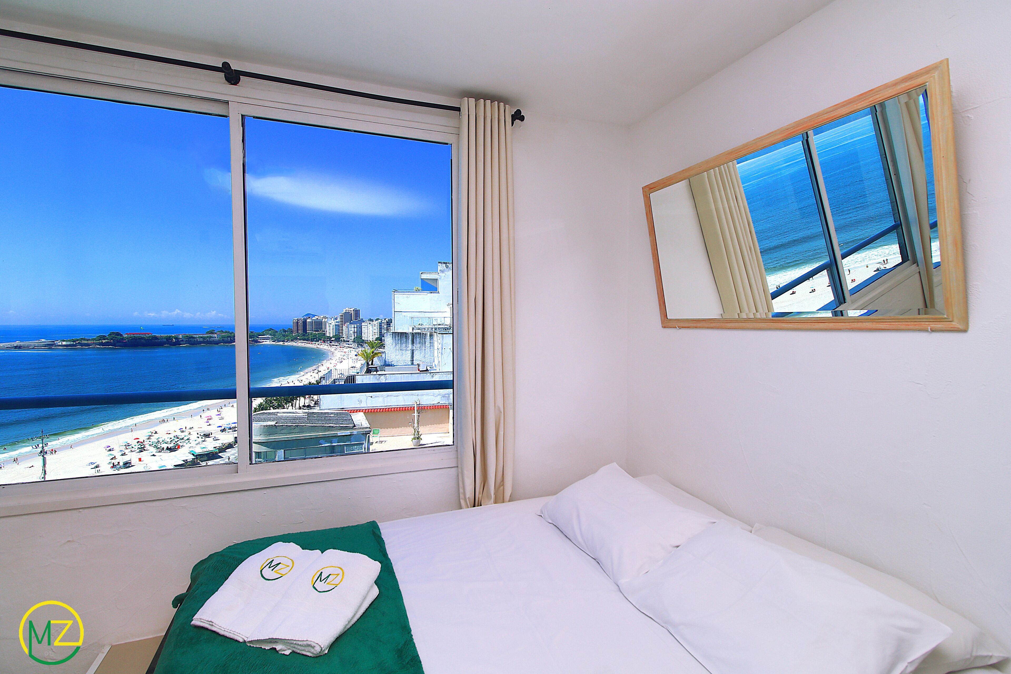 A hotel room with a large window offering a view of the beach and cityscape.
