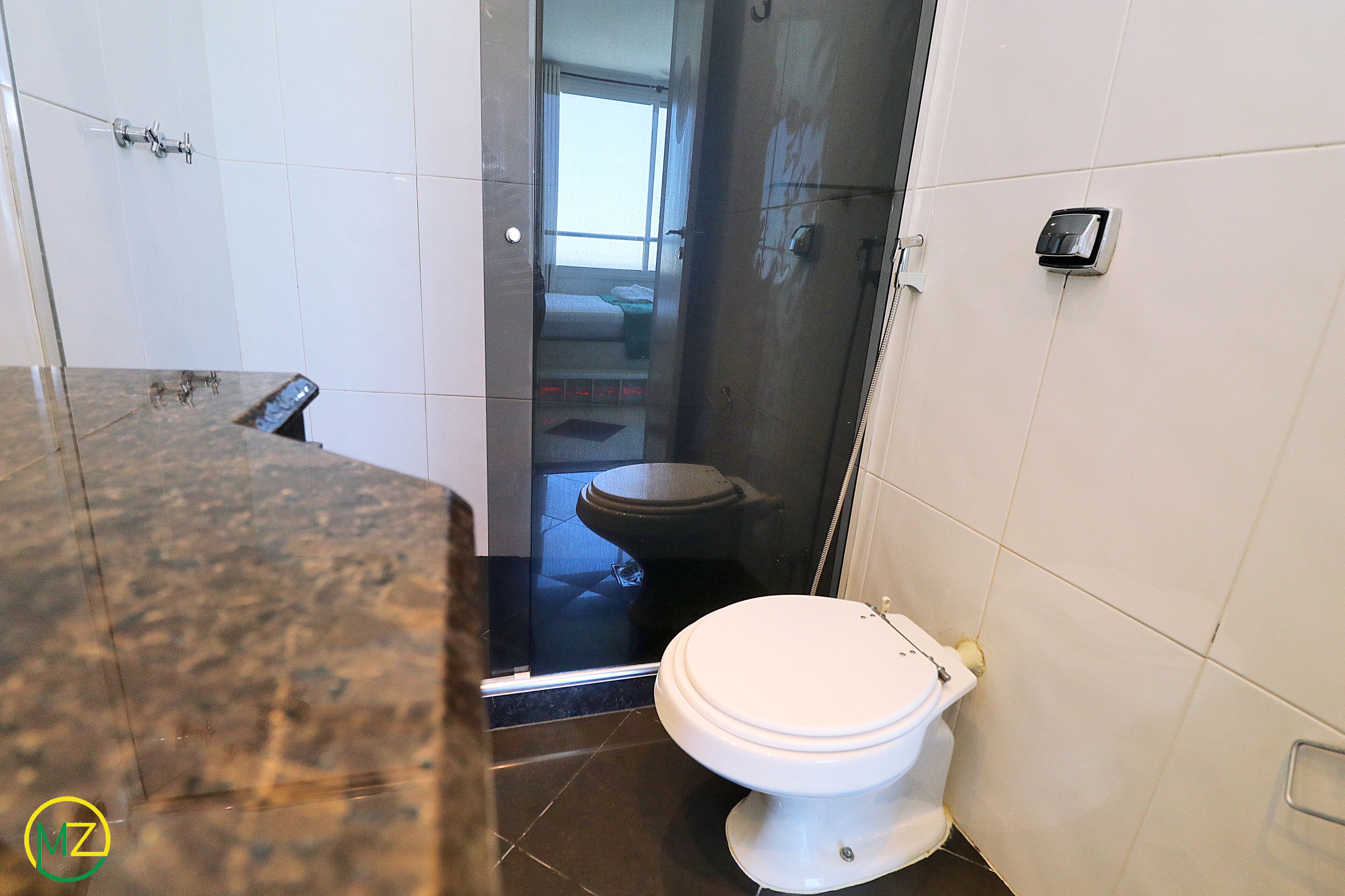 A bathroom with a white toilet, a shower area, and a marble countertop.