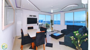 A modern living room with a large TV, a dining area, and a sofa with a view of the sea. - MZapartments Bolivar Penthouse (Rio de Janeiro)