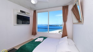 A hotel room with a bed, a ceiling fan, a TV mounted on the wall, and a window with a view of the beach and sea. - MZapartments Bolivar Penthouse (Rio de Janeiro)