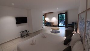 Una habitación de hotel moderna con una cama grande, un televisor de pantalla plana montado en la pared, una mesita y una zona de estar con sofá y sillones.