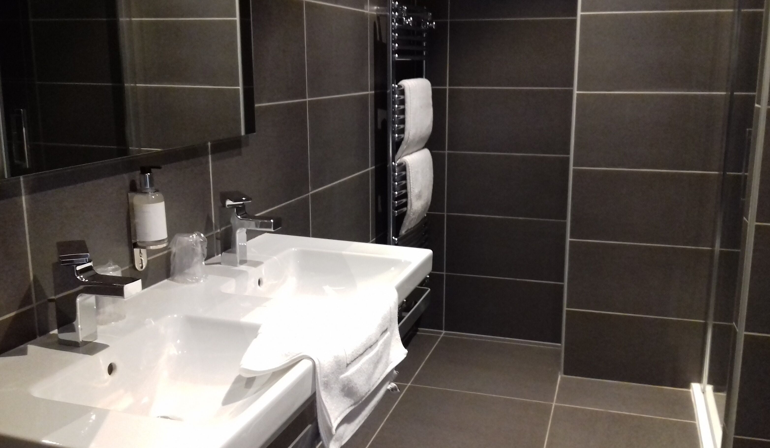 Un baño moderno con dos lavamanos, un espejo grande y un perchero para toallas.