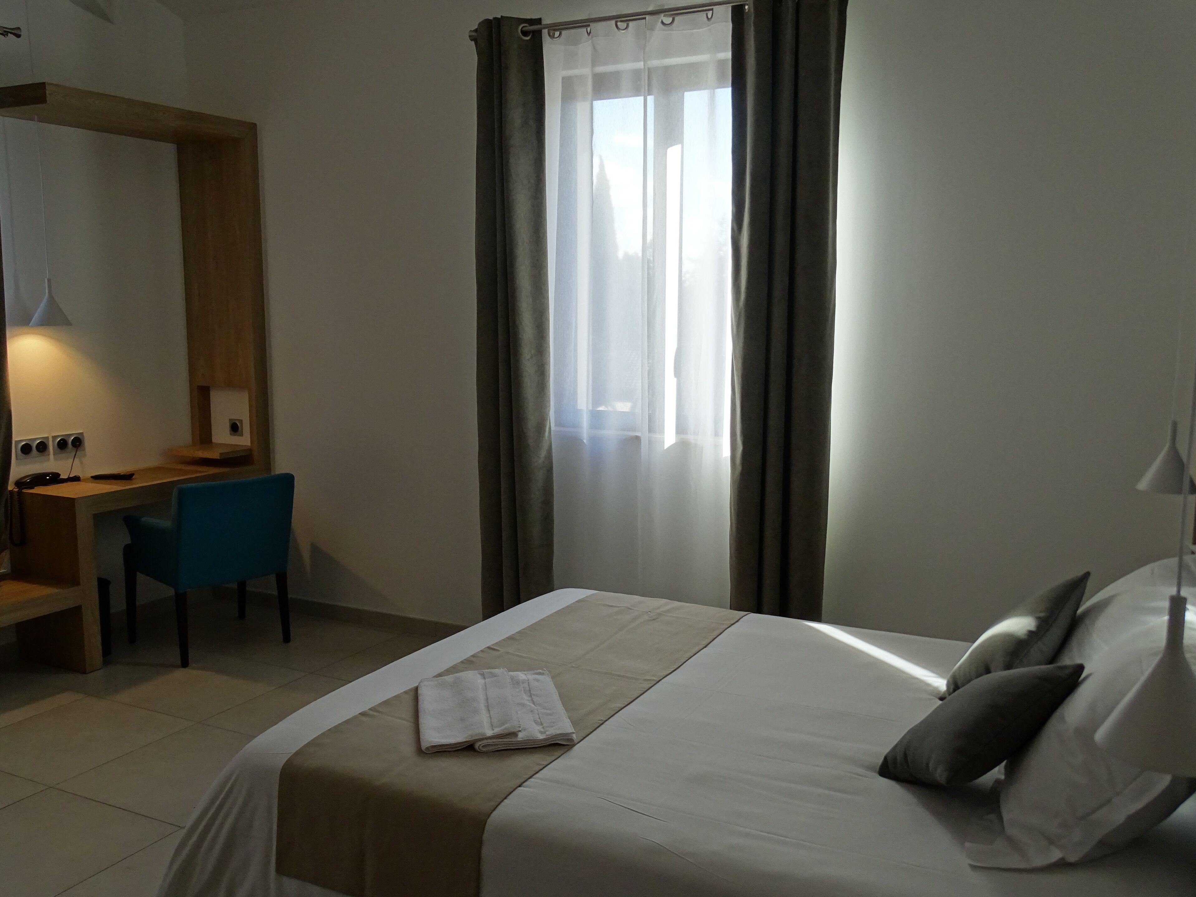 A hotel room with a bed, a desk, a chair, and a window with curtains.