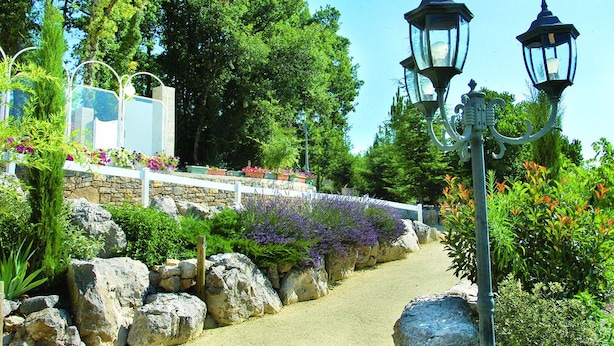 Un sendero en un jardín con muros de piedra, una cerca blanca y flores púrpuras.