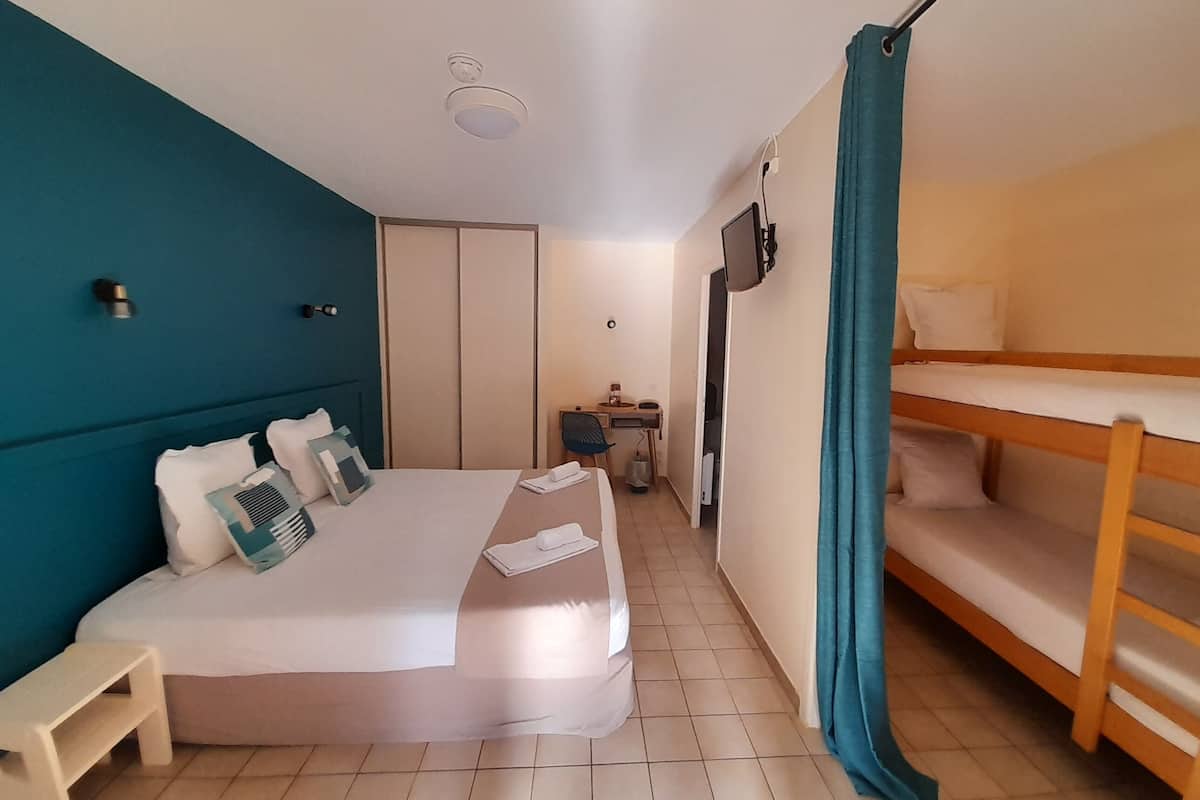 Ein Hotelzimmer mit Bett, Schreibtisch, Sessel, Fernseher und einem Etagenbett.