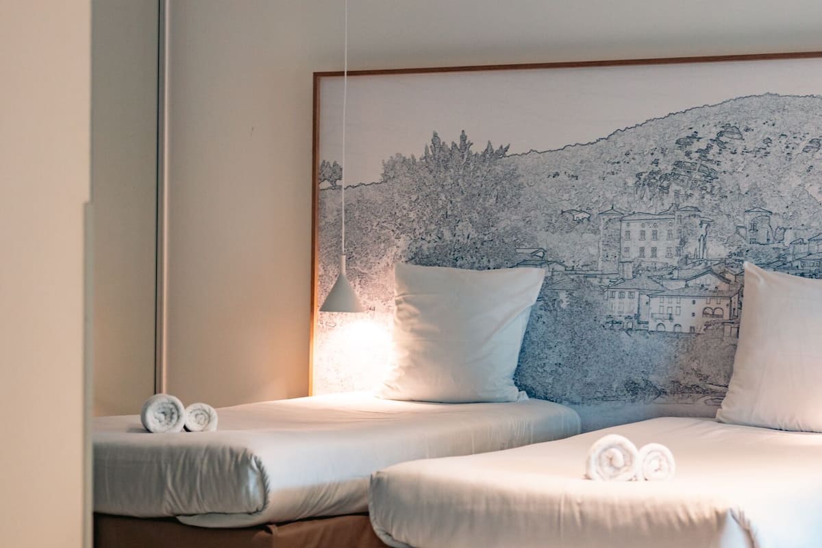 Ein Hotelzimmer mit zwei Betten, einer großen Wandmalerei und einer Pendelleuchte.