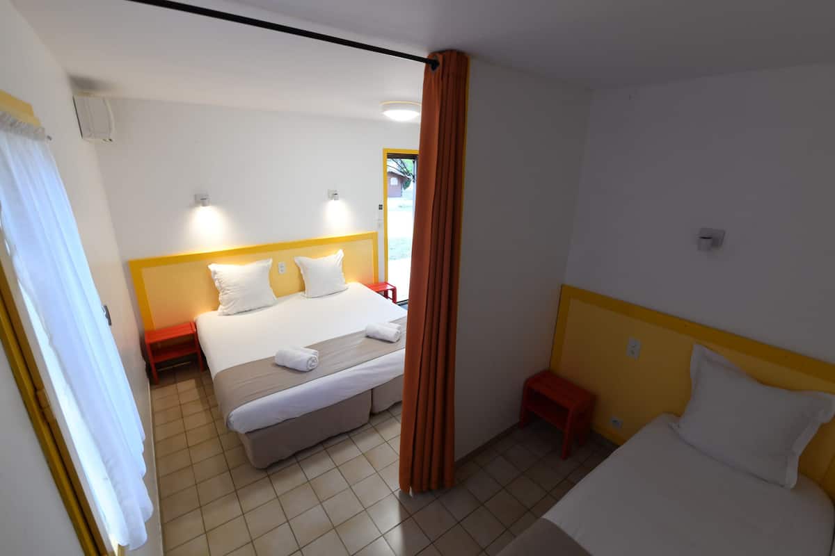 Ein Hotelzimmer mit zwei Betten, einem roten Hocker, einem kleinen Tisch und einem Vorhang.