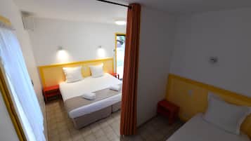 Een hotelkamer met twee bedden, een rode kruk, een tafeltje en een gordijn.