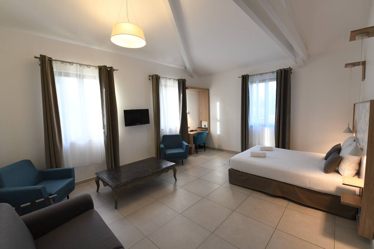 Ein modernes Hotelzimmer mit einem Bett, zwei Sesseln, einem Schreibtisch und einem Fernseher.