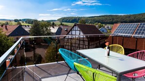 Varanda com guarda-corpo de vidro, vista para uma aldeia com casas tradicionais e painéis solares.