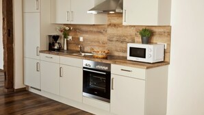 Uma cozinha moderna com armários brancos, coifa de aço inoxidável, forno embutido, micro-ondas e painel de madeira.