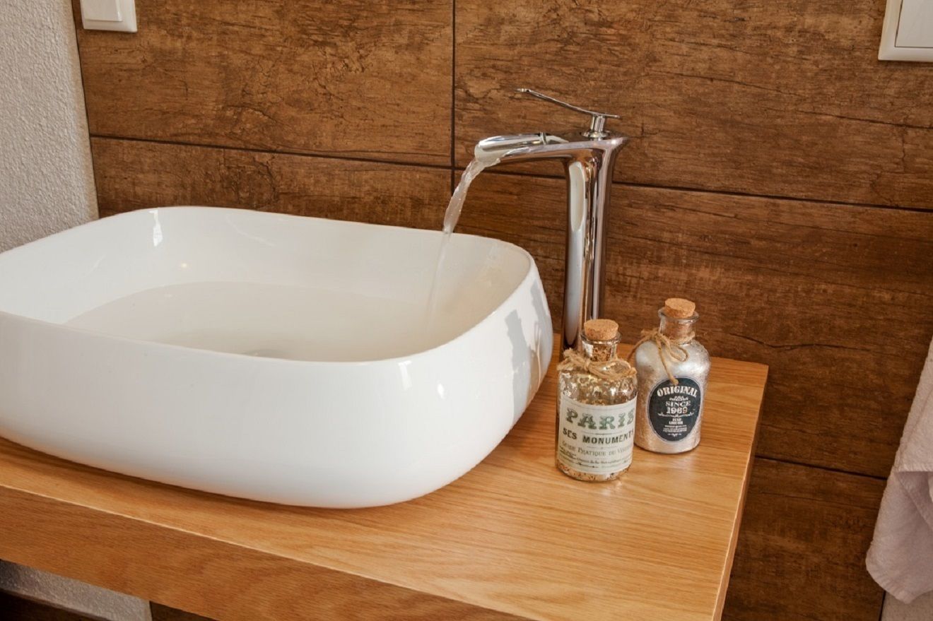 A white sink with running water, two small bottles with labels, and a wooden countertop.