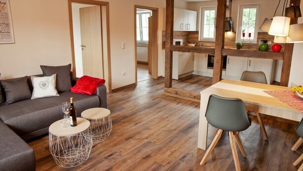 Uma sala de estar moderna com um sofá cinzento, duas mesas redondas e um espaço de refeições com uma mesa de madeira e cadeiras.