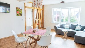 Uma sala de estar moderna com uma mesa de jantar de vidro, cadeiras brancas, um sofá cinzento e uma janela grande.