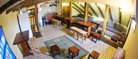 A cozy loft-style living area with wooden beams, a sofa, a dining table, and a kitchen in the background.