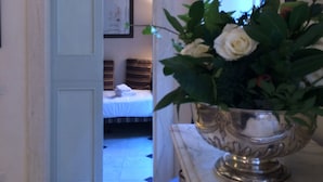 Un pasillo con una consola de mármol que sostiene un florero con flores blancas, que conduce a un dormitorio con una cama y un cuadro en la pared.