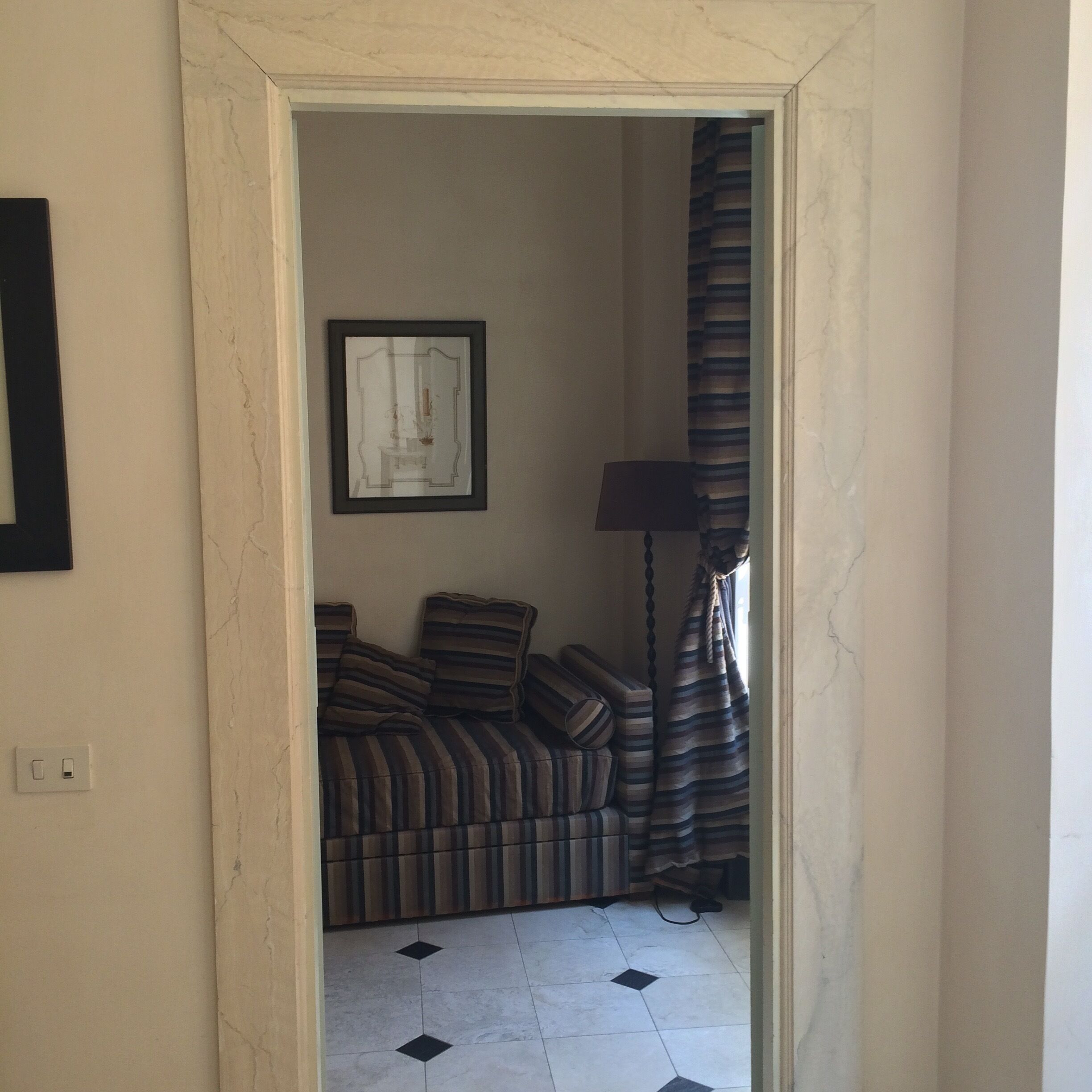 Una puerta que da a una habitación con una cama, un cuadro enmarcado en la pared y una lámpara.