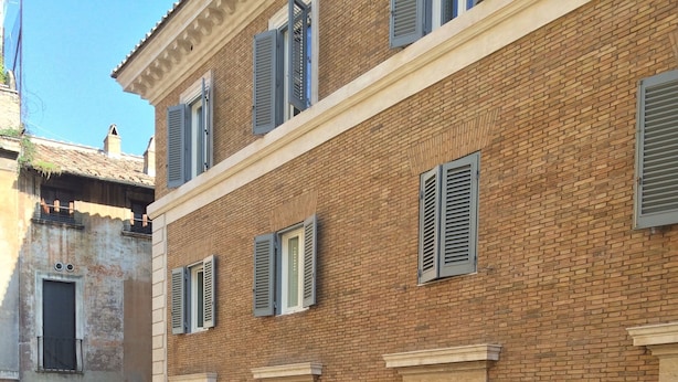 Un edificio de varios pisos con fachada de ladrillo, múltiples ventanas con contraventanas y detalles de piedra decorativa.