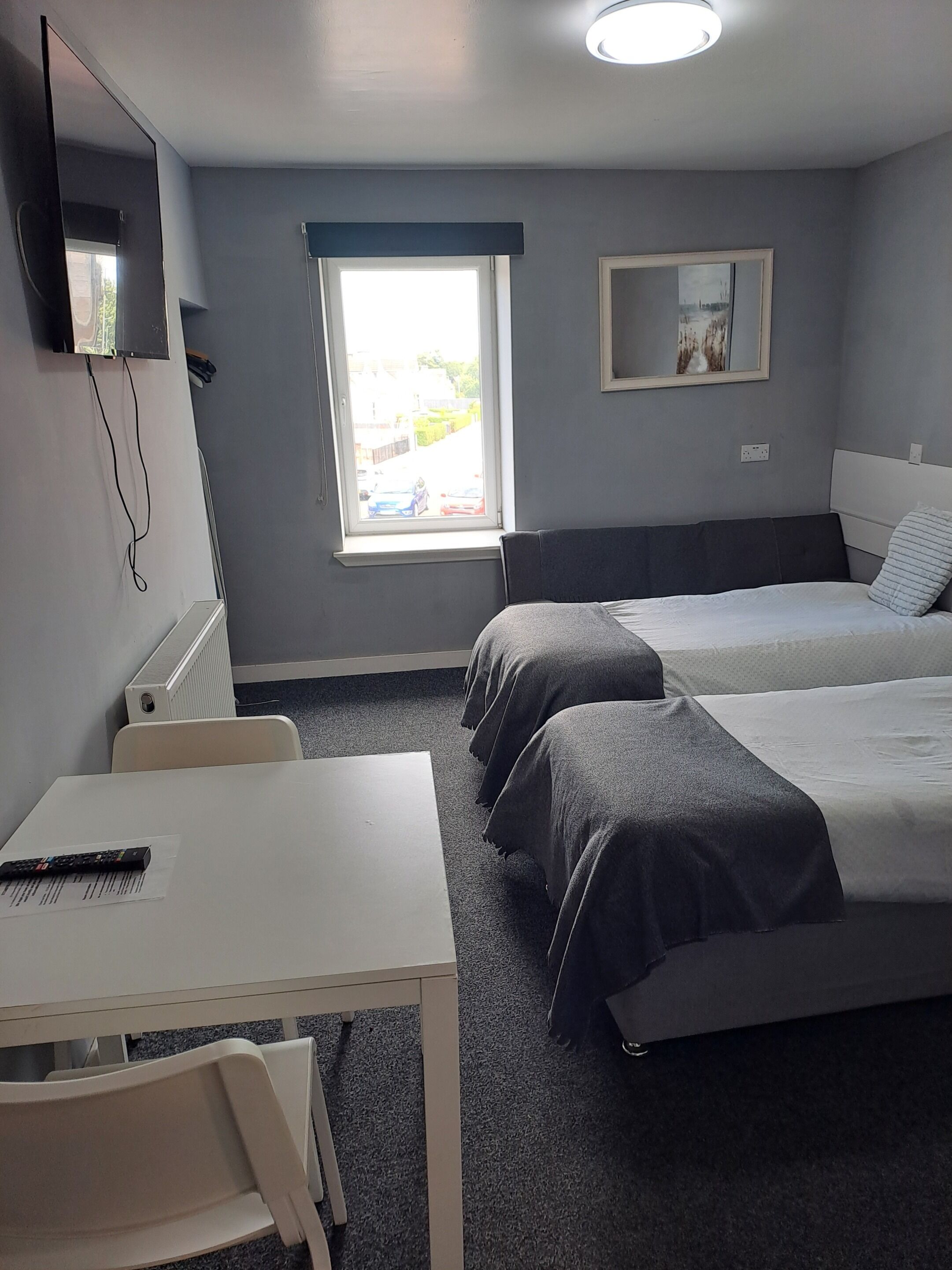 Una camera d'albergo con due letti, una scrivania, una sedia, un televisore montato a parete e una finestra vista esterna.