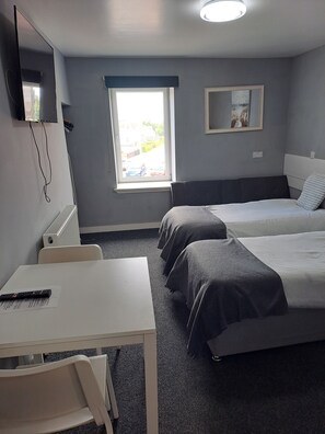 A hotel room with two beds, a desk, a chair, a TV mounted on the wall, and a window with a view of the outside. - Stonefield Rooms (Glasgow)