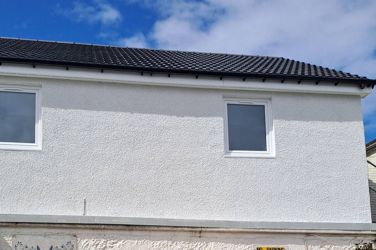 Un bâtiment à deux étages, doté d’une façade blanche à texture et d’un toit recouvert de tuiles sombres.