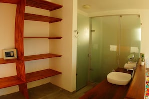 A bathroom with a glass shower door, a white sink, and wooden shelves. - Spondylus Beach House I (Los Organos)