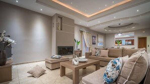 A modern living room with a sofa, coffee table, and a fireplace. - Ostria Luxury Villa (Zakynthos)