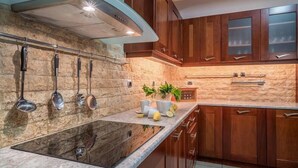 A kitchen with a stone backsplash, wooden cabinets, and a stainless steel range hood. - Ostria Luxury Villa (Zakynthos)