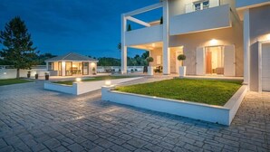 A modern two-story house with a paved driveway, outdoor seating area, and a well-maintained lawn. - Ostria Luxury Villa (Zakynthos)