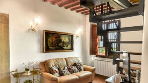 Ein Wohnzimmer mit einem beigefarbenen Sofa, einem Gemälde, einem goldgerahmten Beistelltisch mit Pflanze und einem Fernseher auf einem Holzboden.
