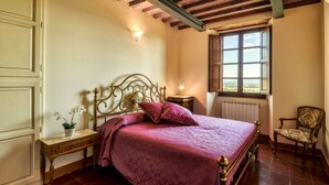 Ein Schlafzimmer mit Bett, Nachttisch, Lampe, Stuhl und Fenster mit Blick.