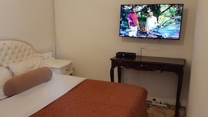 A hotel room with a bed, a television mounted on the wall, a bedside table, and a small wooden nightstand. - KaRwizi  (Harare)