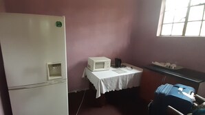 A small room with a white refrigerator, a microwave, a table with a white tablecloth, and a window. - KaRwizi  (Harare)